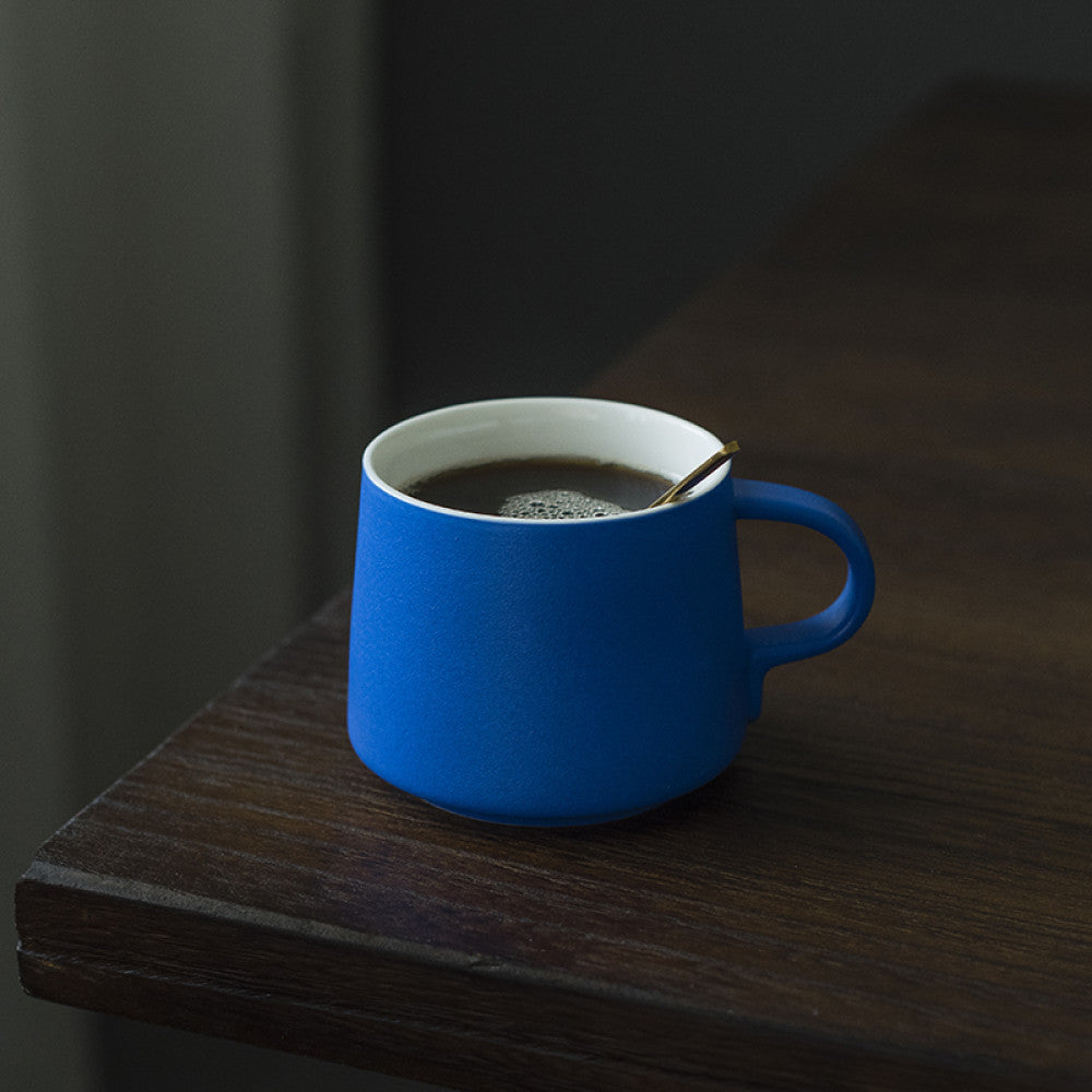 Kobaltblaue Porzellantasse mit schwarzem Kaffee auf Tischkante – modern, robust und stilsicher.