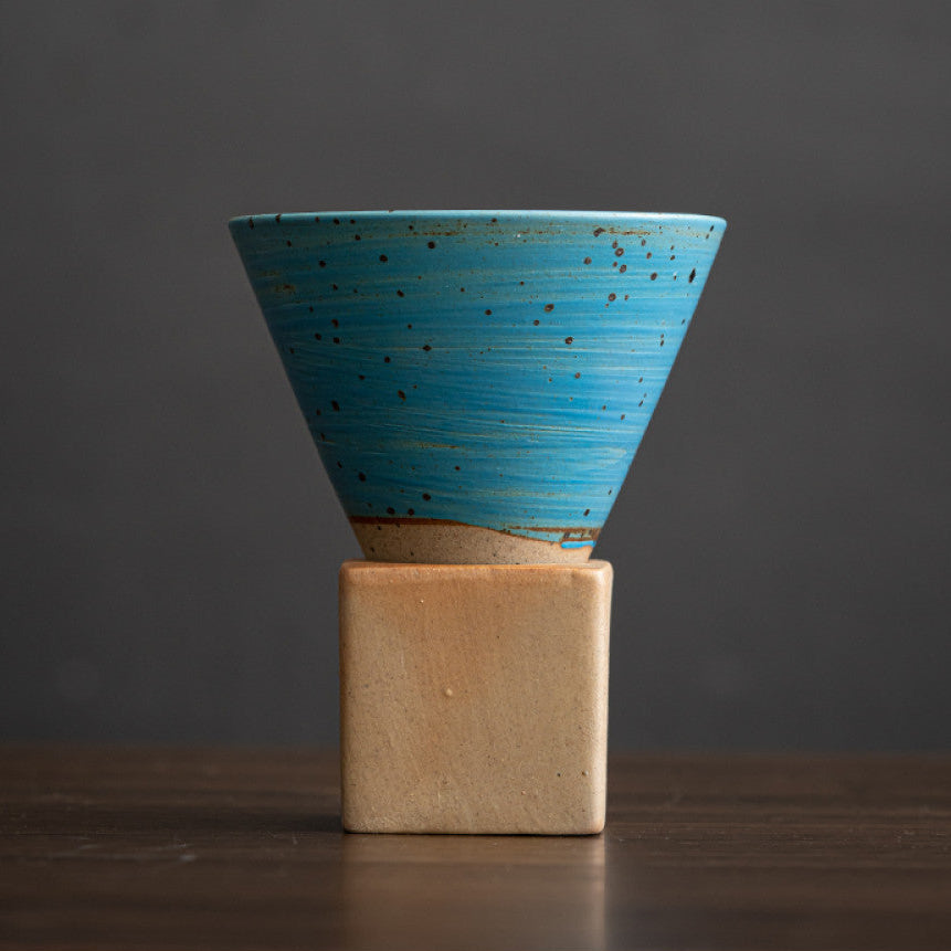 Konische Keramiktasse mit leuchtend blauer Glasur und feinen Sprenkeln auf naturfarbenem Sockel. Die minimalistische Tasse kombiniert modernes Farbspiel mit traditioneller Handwerkskunst im japanischen Stil. Ideal für Kaffee oder Tee.