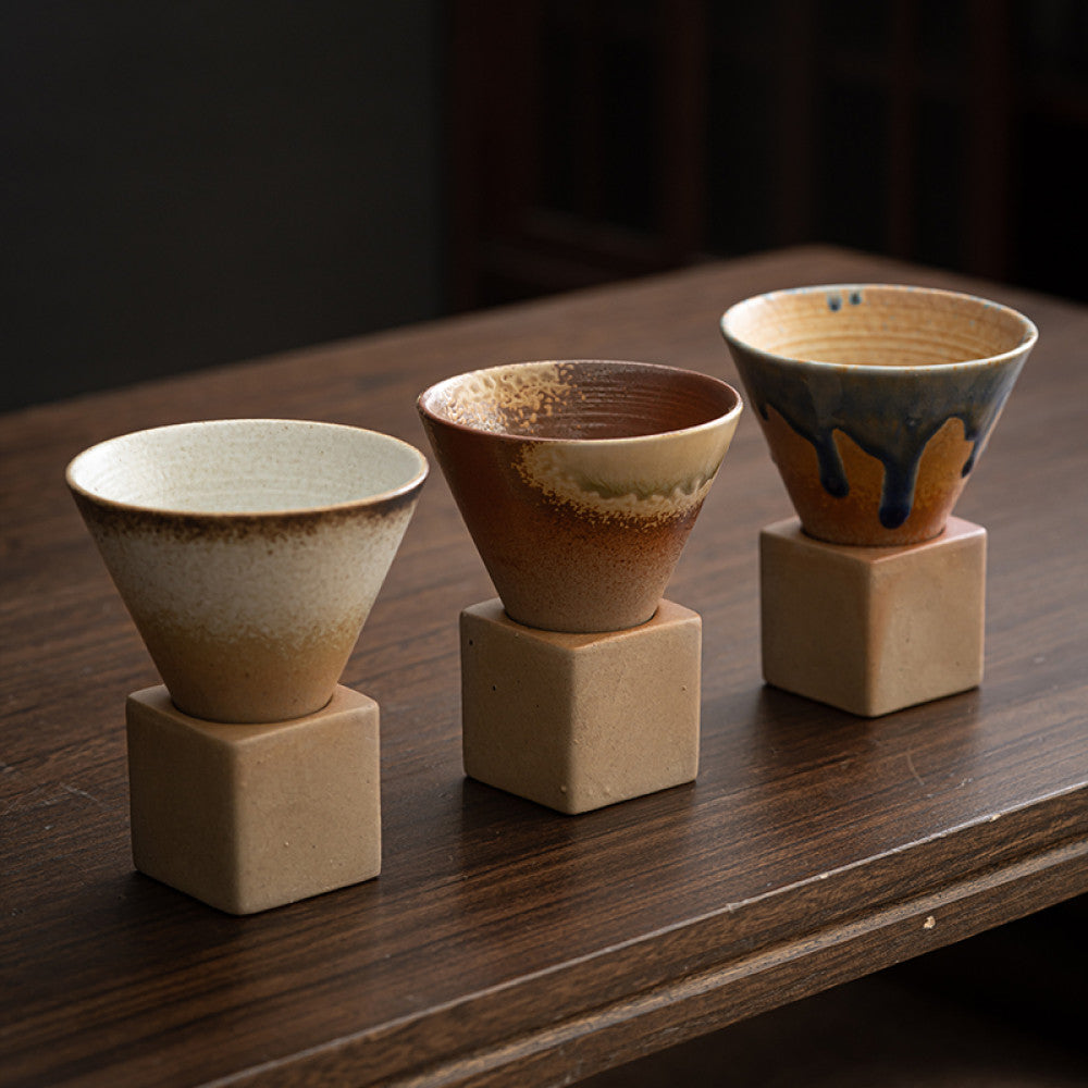 Handgemachte Kaffeetasse aus Grobkeramik im japanischen Retro Stil. Kreative Espressotasse mit konischer Form und minimalistischer Ästhetik. Perfekt für alle Arten von Kaffee. Steht auf kubischer Keramikbasis. Ideal für stilvolle Kaffeerituale und moderne Interior Designs.