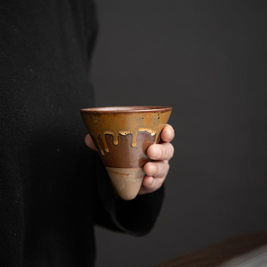 Person hält handgemachte Keramiktasse mit brauner Glasur und heller Tropfenoptik. Die konische Form liegt gut in der Hand und unterstreicht das japanische Retro Design. Ideal für Latte oder Espresso.