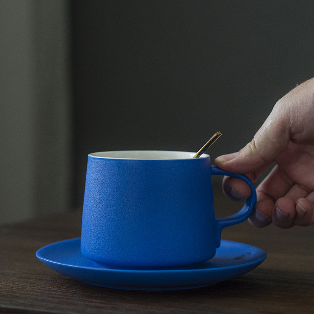 Hand hält eine japanisch inspirierte blaue Porzellantasse mit goldenem Löffel – stilvoller Begleiter für moderne Tischkultur.