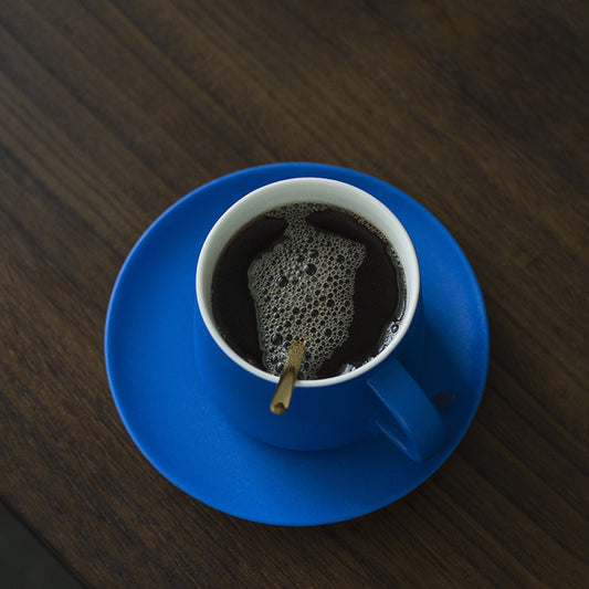 Obenansicht einer blauen Porzellantasse mit dunklem Kaffee und goldenem Löffel – cleanes Design trifft auf Funktionalität.