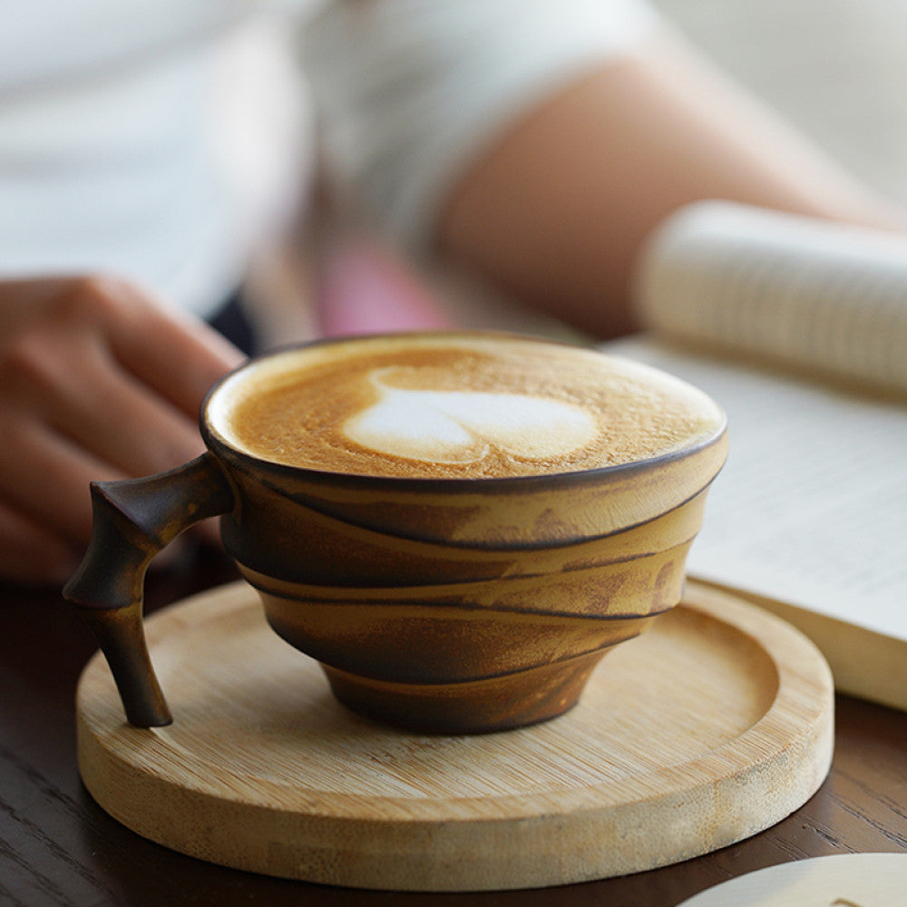 Kreative Keramiktasse mit auffälligem Elefantenhenkel, serviert mit Latte Art auf einem runden Holzuntersetzer.