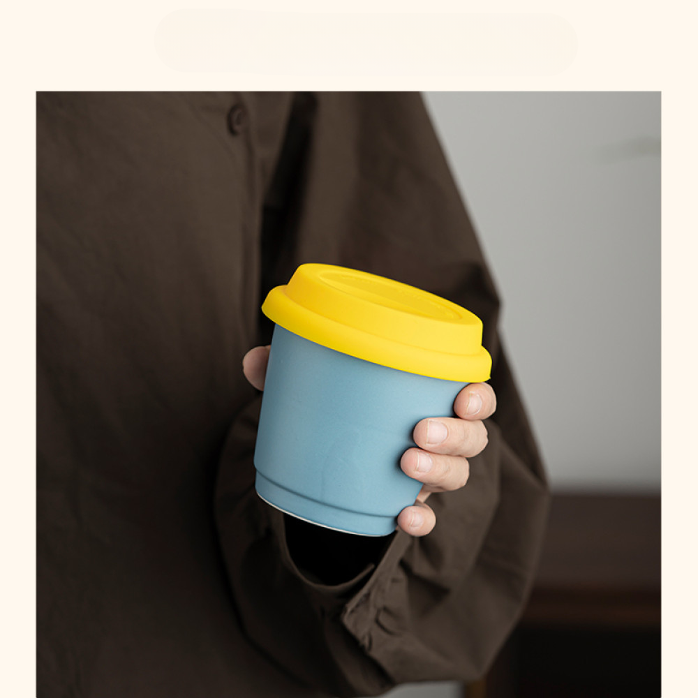 Wiederverwendbarer Mug to Go in Hellblau mit gelbem Deckel, in der Hand gehalten – ideal für stilvollen Kaffee unterwegs.