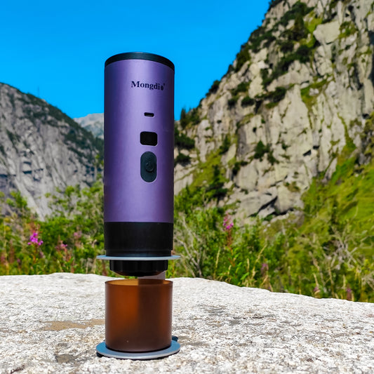 Lila portable Kaffeemaschine von Honeybean auf einem grossen Stein, dahinter beeindruckende Bergkulisse in der Schweiz – ideal für Kaffee unterwegs in der Natur.