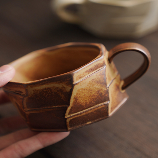 Braune Tasse mit markanter Textur in der Hand gehalten. Individuell gefertigte Keramik mit warmem Ton.