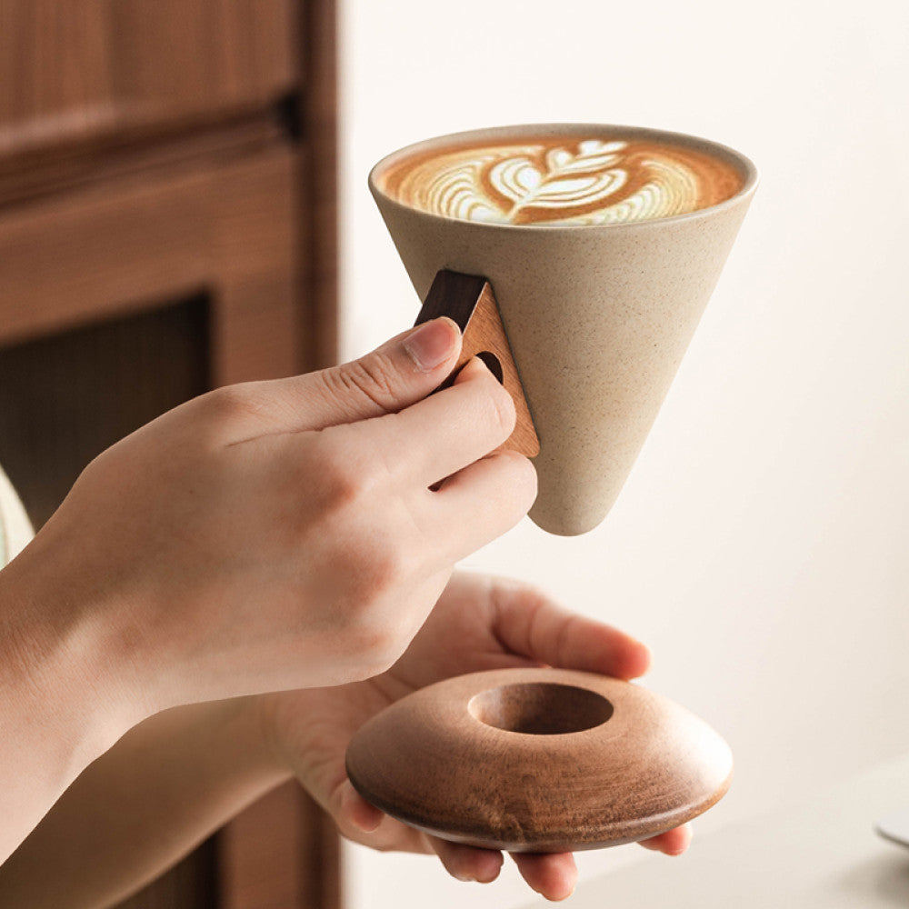 Keramiktasse im konischen Design mit Latte Art, stilvoll in der Hand serviert – auf rundem Holzunterteller.