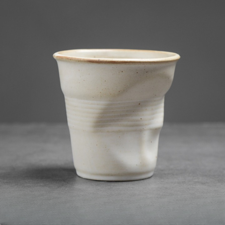 Weisse Keramiktasse mit organischer Oberfläche auf grauem Hintergrund. Ideal für puristische Wohnkonzepte.