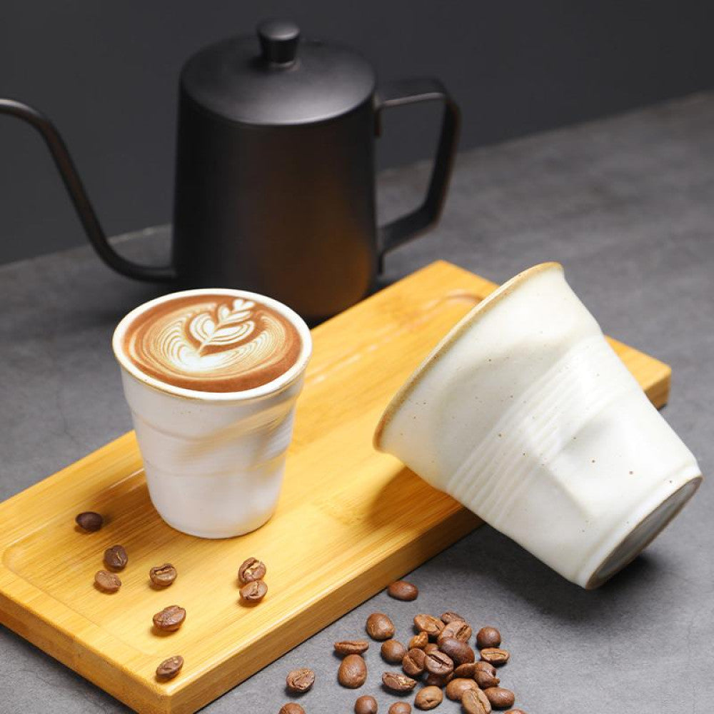 Zwei weisse Keramiktassen mit Kaffeebohnen und Latte Art auf einem Holzbrett. Stilvolle Präsentation für Kaffee-Liebhaber.