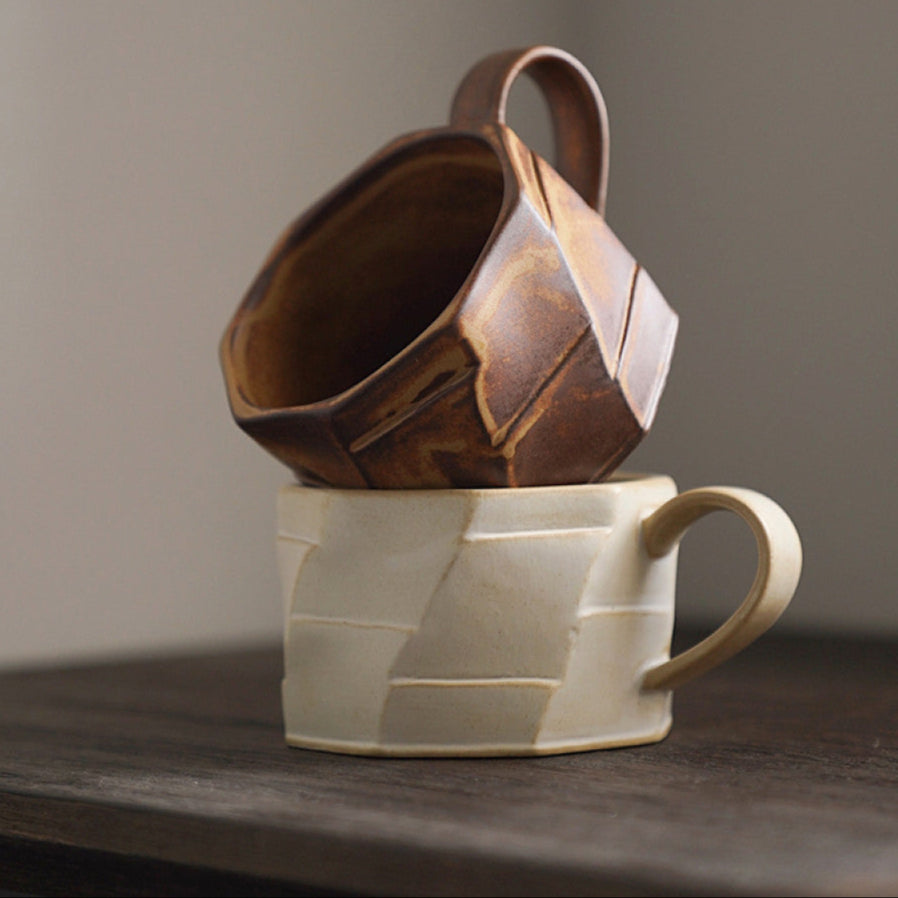 Zwei strukturierte Keramiktassen in Beige und Braun, kunstvoll aufeinander gestapelt. Handmade-Charakter mit stilvoller Formgebung.