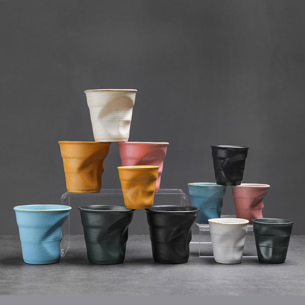 Mehrere bunte Keramiktassen mit Knickdetail als farbenfroher Stapel arrangiert. Ideal als modernes Tassen-Set für Kaffee oder Tee.