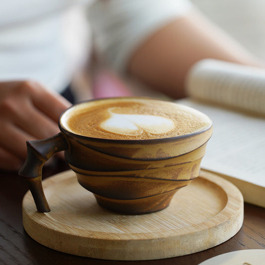 Kreative Keramiktasse mit auffälligem Elefantenhenkel, serviert mit Latte Art auf einem runden Holzuntersetzer.