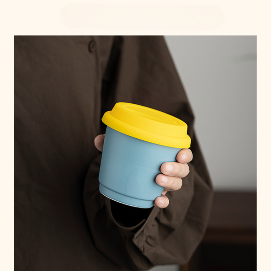 Wiederverwendbarer Mug to Go in Hellblau mit gelbem Deckel, in der Hand gehalten – ideal für stilvollen Kaffee unterwegs.