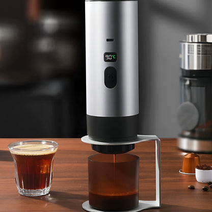 Silberne portable Kaffeemaschine mit 90 °C-Anzeige beim Brühen eines Espressos, daneben ein Glas frisch gebrühter Kaffee und Kapseln auf einem Holztisch.