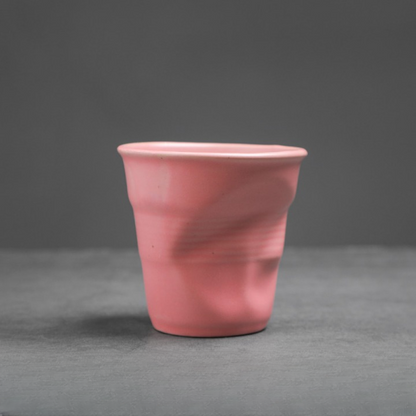 Zarte rosa Tasse mit matter Glasur und organischem Knickmuster. Sanftes Design für stilvolle Kaffeepausen.