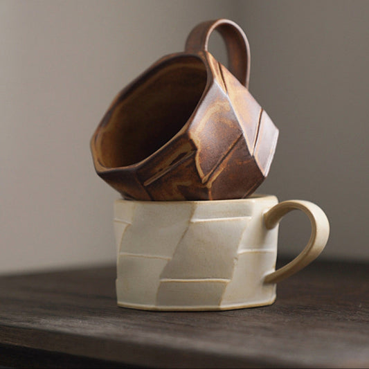 Zwei strukturierte Keramiktassen in Beige und Braun, kunstvoll aufeinander gestapelt. Handmade-Charakter mit stilvoller Formgebung.