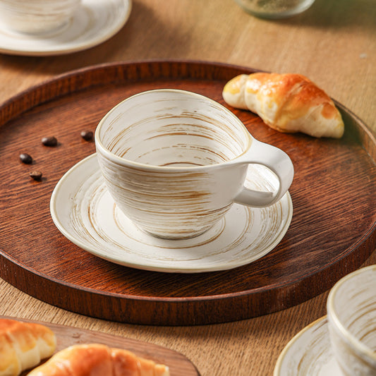 Handgemachte Vintage-Kaffeetasse aus Keramik mit passender Untertasse auf Holztablett, neben Croissant – ideal für stilvolle Kaffeezeremonien.