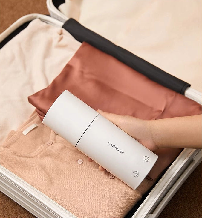 Hand hält einen weissen, tragbaren Wasserkocher über einem offenen Koffer mit ordentlich gefalteter Kleidung – ideal für Reisen.